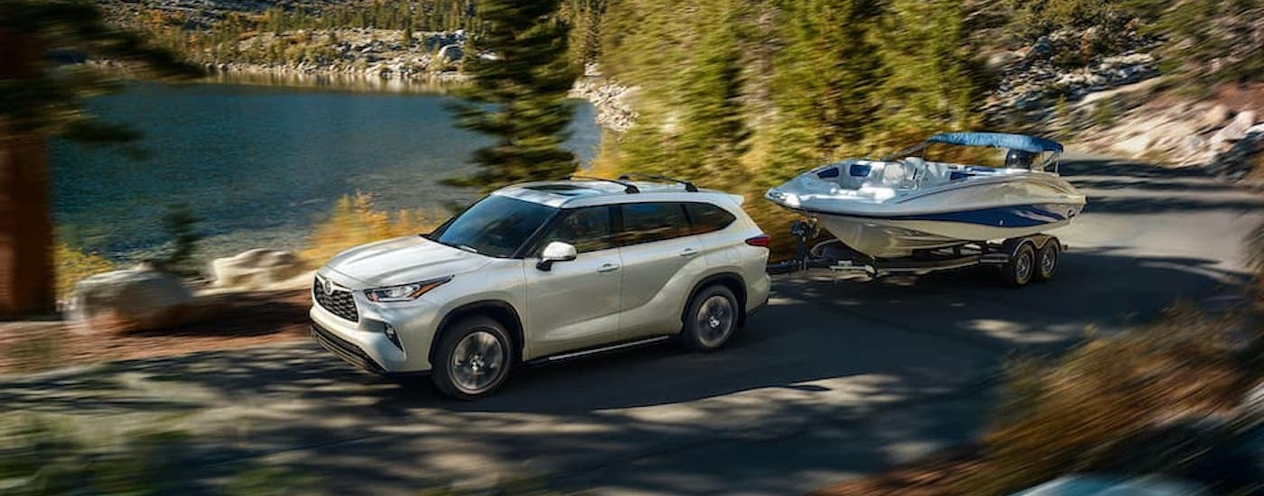A white 2020 Toyota Highlander is shown from the side while towing a boat.