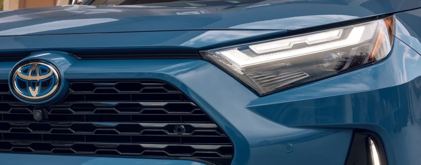A close up of the grille and headlight on a blue 2024 Toyota RAV4 XSE Hybrid is shown.