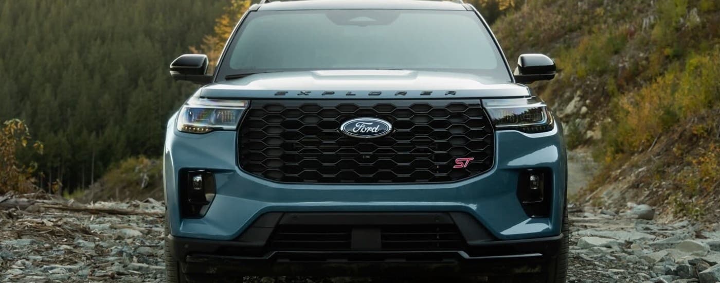 A close up of a blue 2025 Ford Explorer ST is shown from the front parked on a trail.