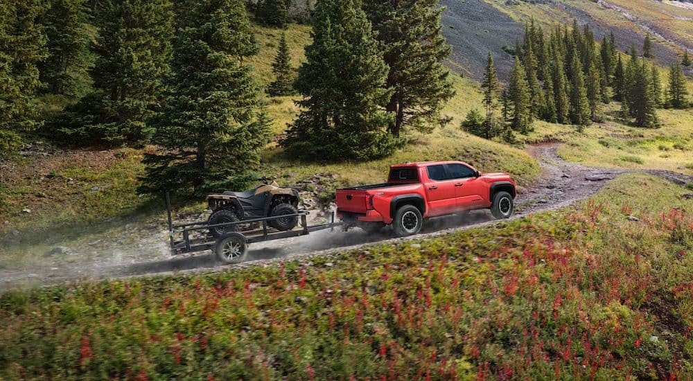 A red 2024 Toyota Tacoma TRD Off-Road os shown from the side while towing an ATV.