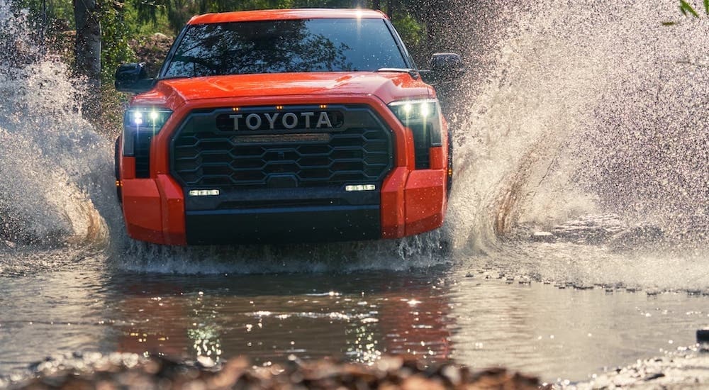 An orange 2022 Toyota Tundra TRD is shown from the front while driving through mud.