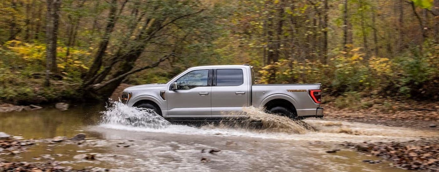 A silver 2021 Ford F-150 is shown from the side while driving through a creek after leaving a dealer that has used cars for sale in Westminster.