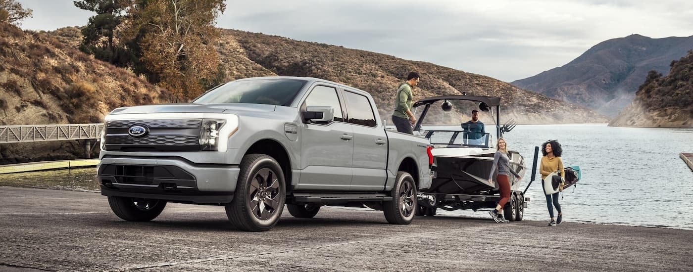 A grey 2024 Ford F-150 Lightning is towing a boat out of a lake.