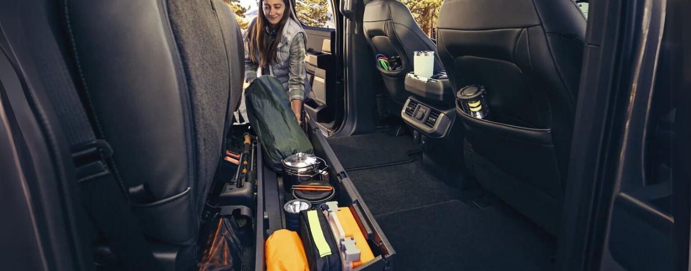 A person is shown stowing camping gear in a 2022 Ford F-150 Lightning for sale.