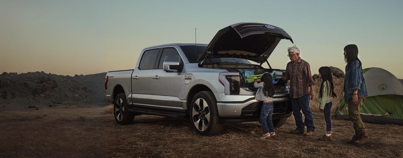 A silver 2023 Ford F-150 Lightning is shown at a campsite.