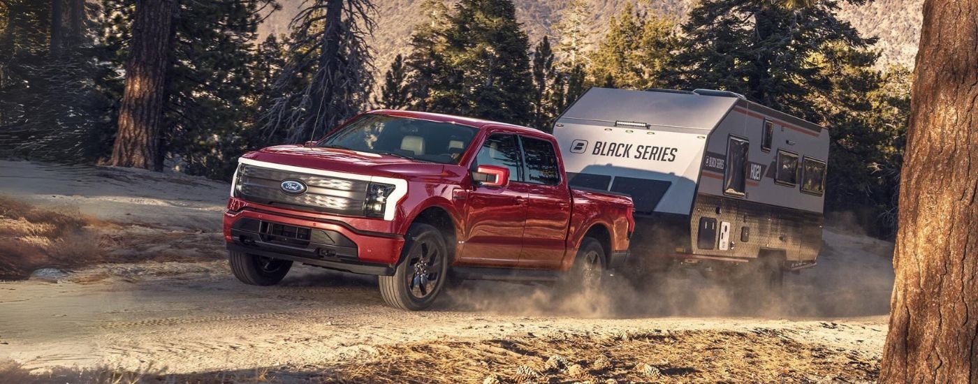 A red 2023 Ford F-150 Lightning is shown towing a trailer on a dirt path.
