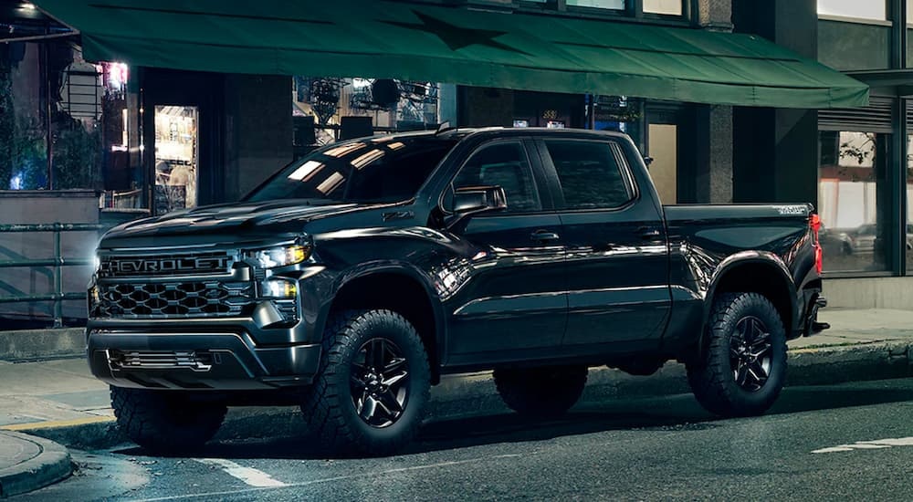 A black 2023 Chevy Silverado 1500 Z71 Trail Boss is shown from the side on a city street after leaving a dealer that has used trucks for sale near Keene.