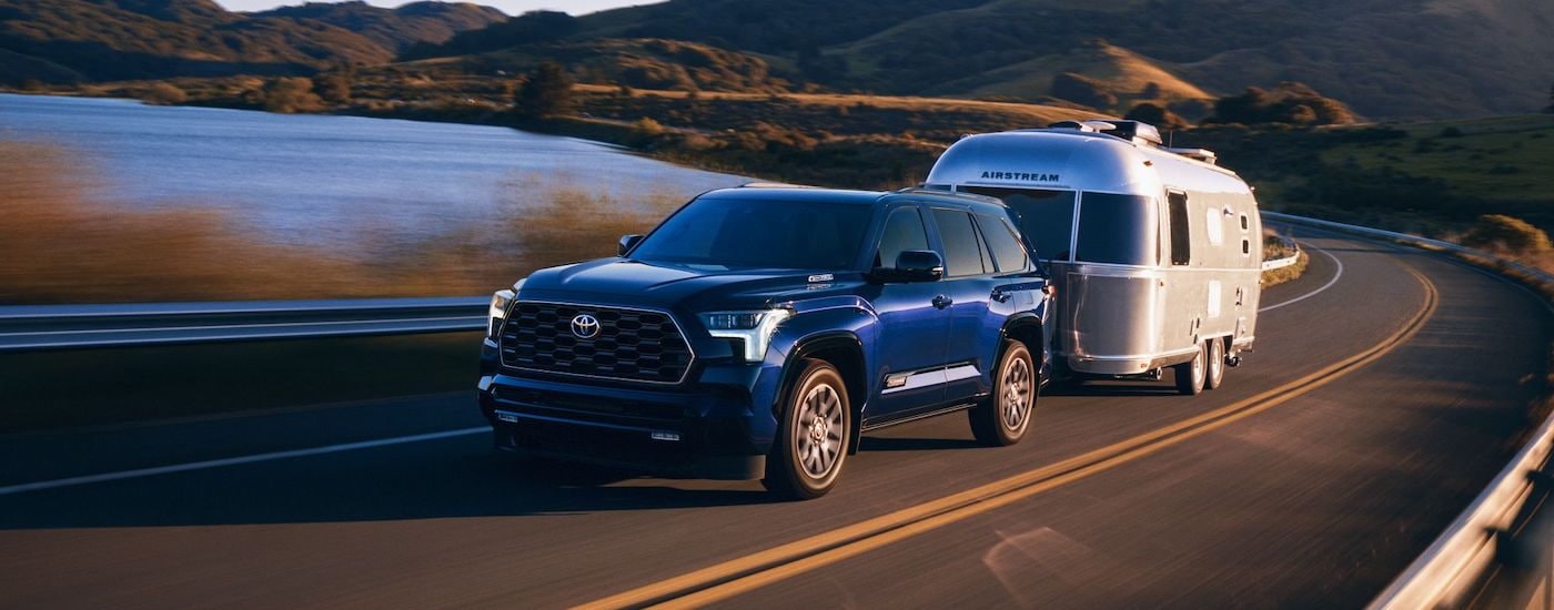 A blue 2024 Toyota Sequoia is shown from the front at an angle while towing a camper after leaving a Toyota dealer near Chesterfield.