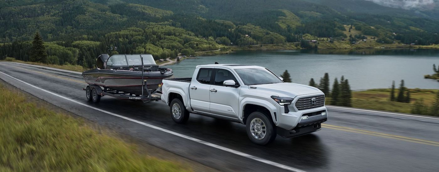 A white 2024 Toyota Tacoma is shown towing a boat.