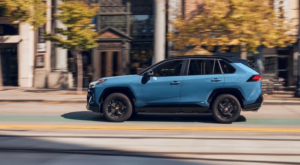 A blue 2024 Toyota RAV4 Hybrid is shown driving on a city street.