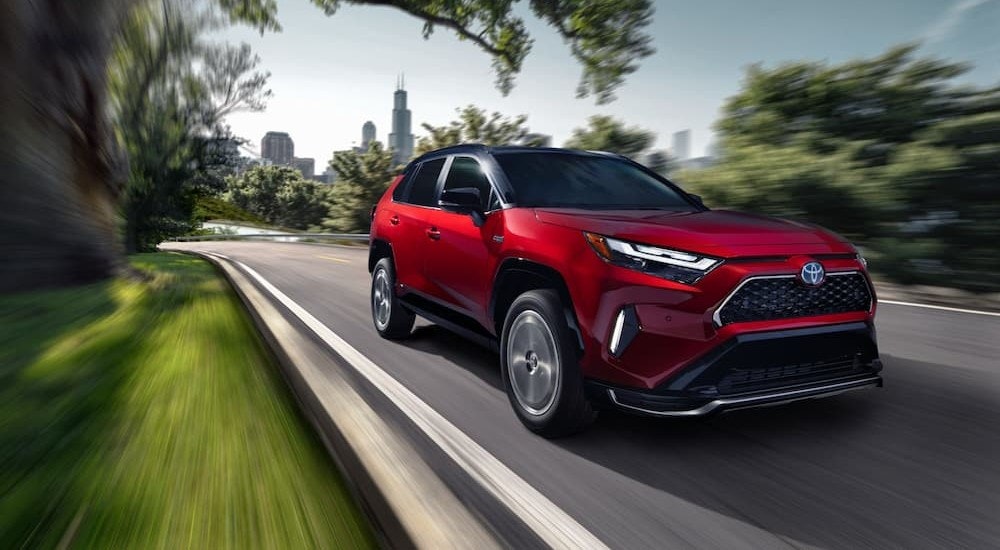 A red 2024 Toyota RAV4 Prime is shown driving to a Toyota dealer near Greenfield.