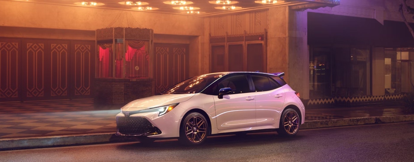 A white 2025 Toyota Corolla Hatchback Nightshade parked under a theater marquee at night.