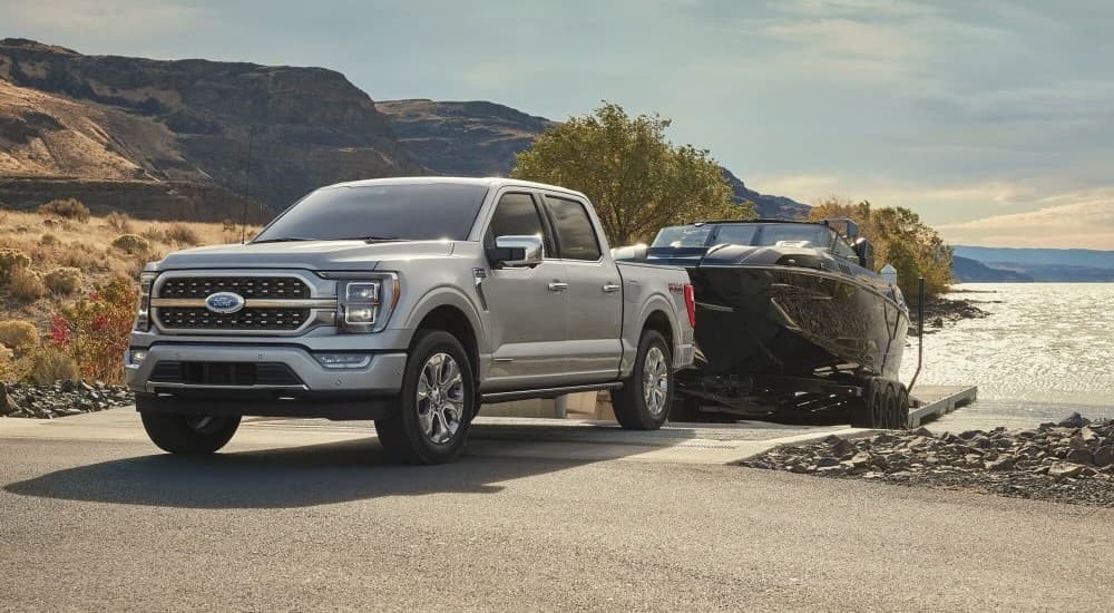 A silver 2024 Ford F-150 towing a boat out of a lake.