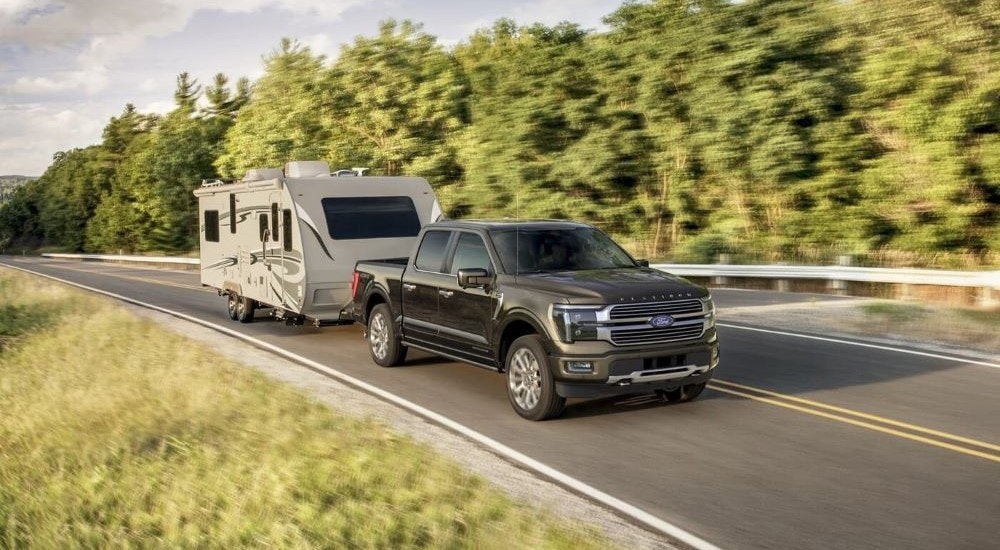 A black 2024 Ford F-150 Platinum Plus towing a camper from a Ford dealer near Rutland.