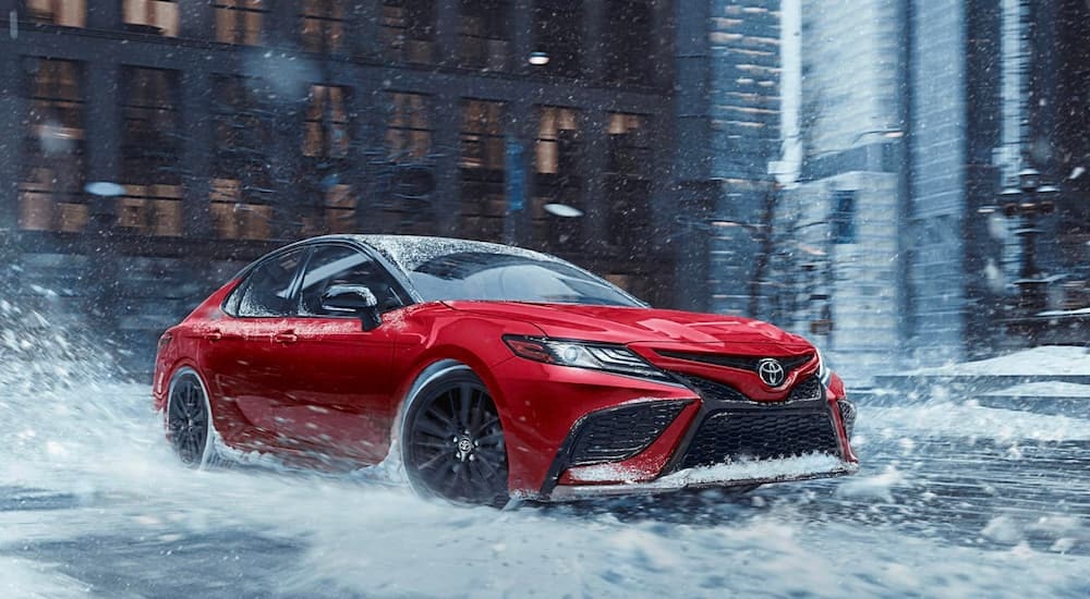 A red 2020 Toyota Camry driving through a snowy city intersection.