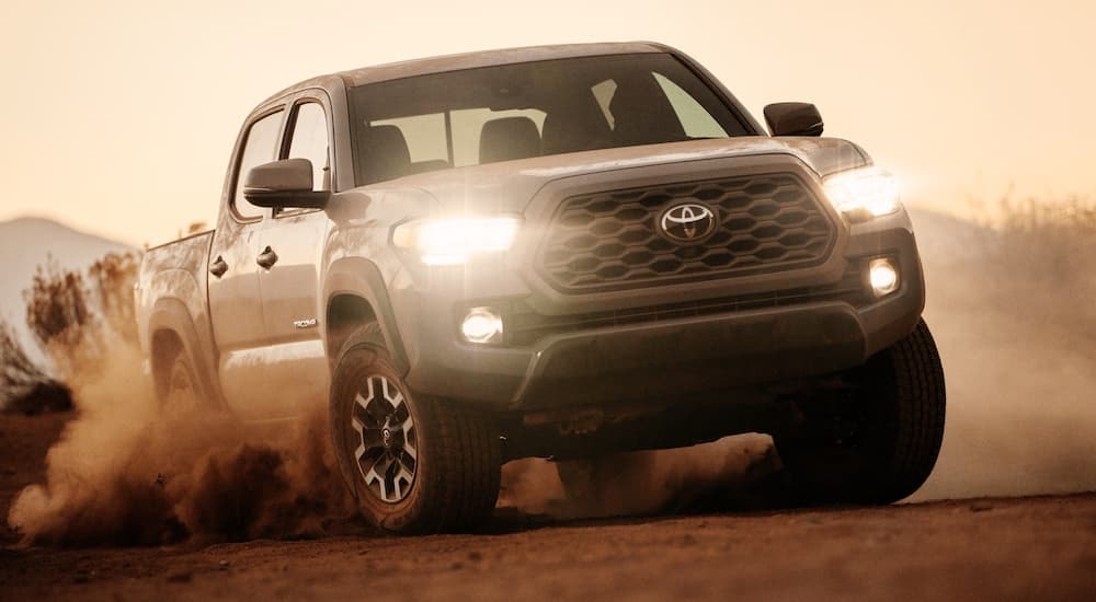 A white 2020 Toyota Tacoma driving off-road over a dirt hill.