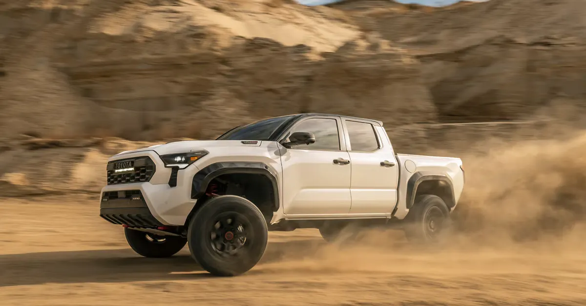 2026 Toyota Tacoma TRD Pro driving off road through a dusty desert trail with rugged terrain in the background.