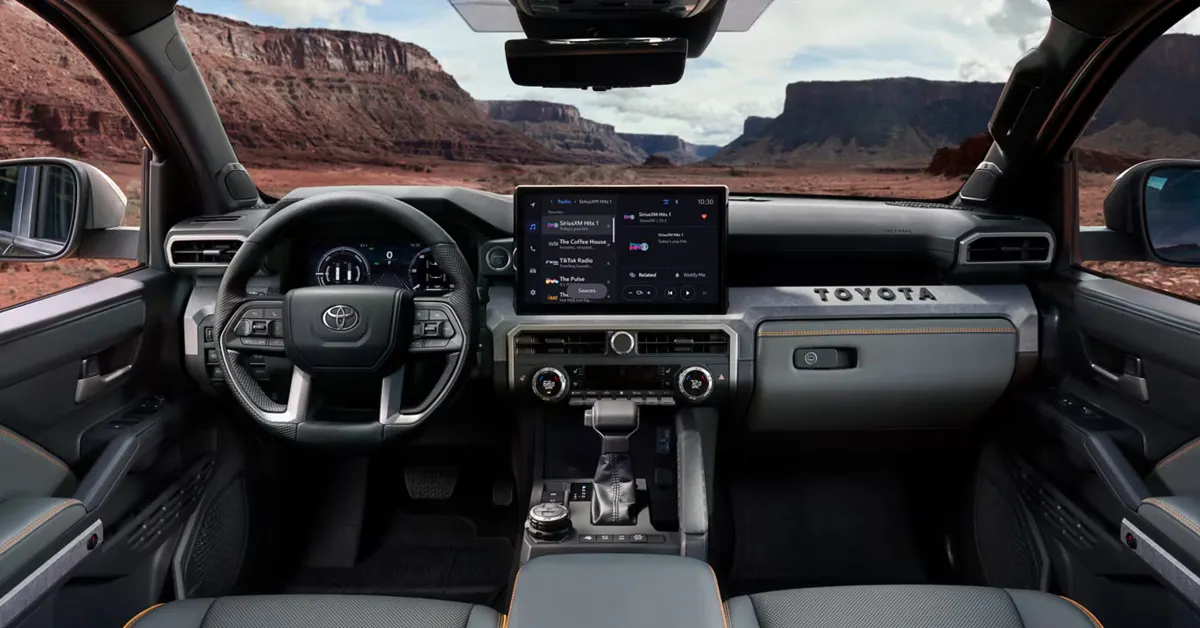 2026 Toyota Tacoma cabin from the back seat, featuring a leather-wrapped steering wheel, fully digital instrument cluster, large center touchscreen infotainment display