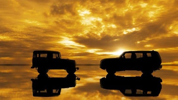 two vehicles under a yellow sky and glassey lake