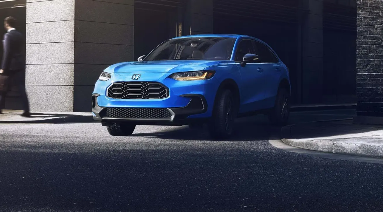 Blue Honda HR-V SUV driving out of a shaded urban parking area with its front grille and LED headlights visible.