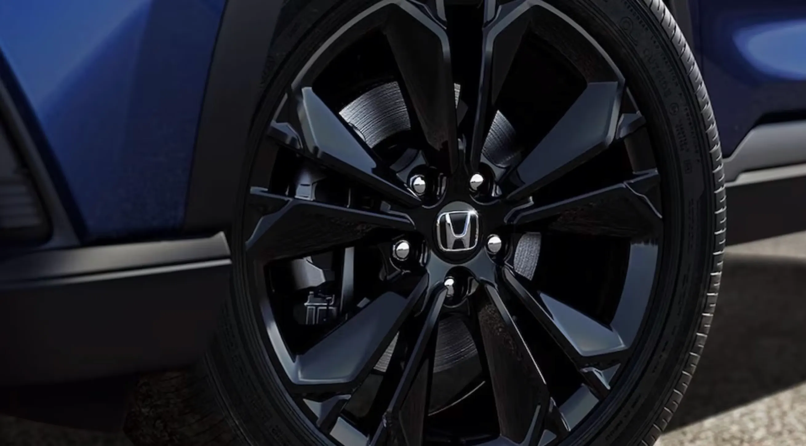 Detailed close-up of a black multi-spoke Honda alloy wheel and tire mounted on a blue SUV with visible brake components.