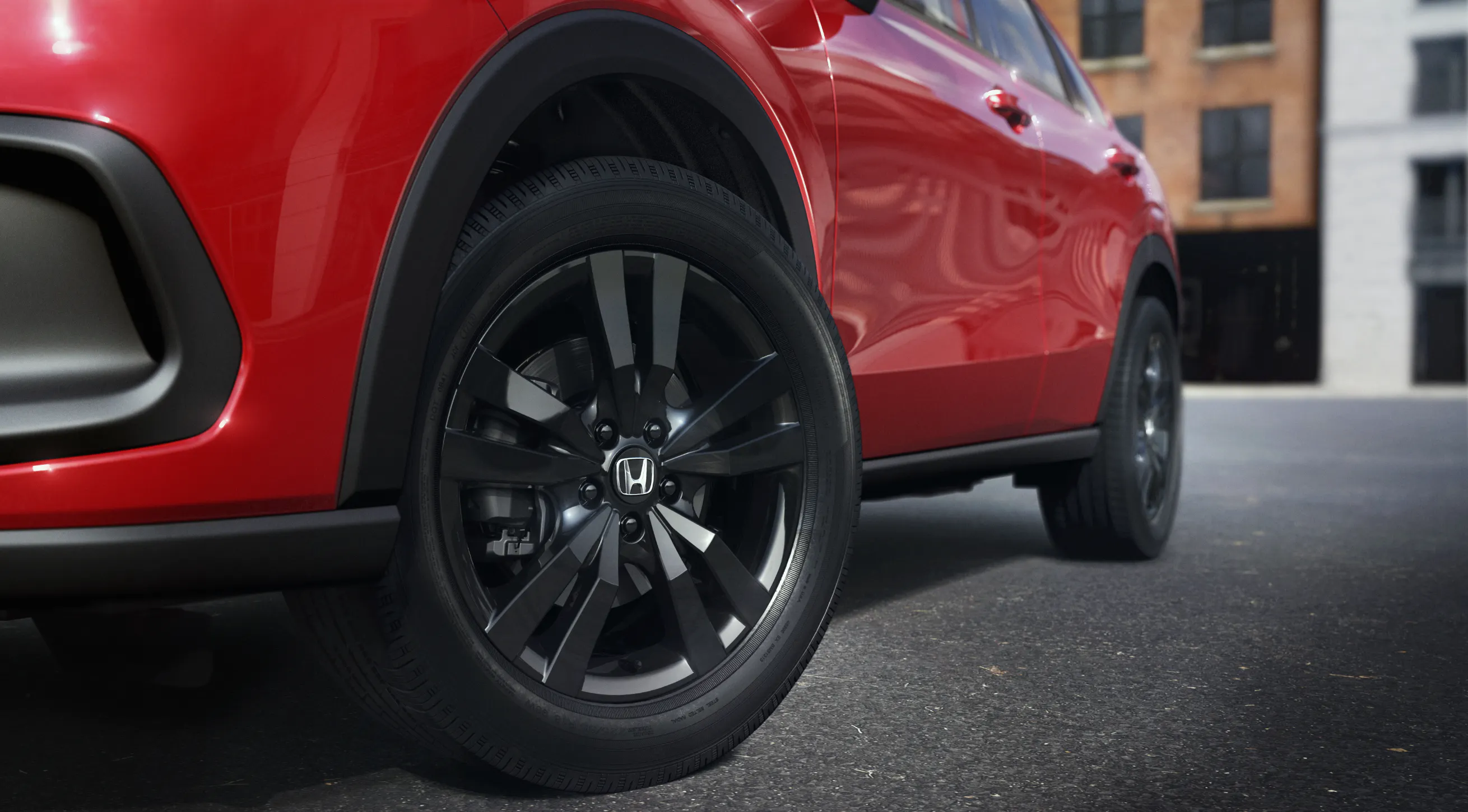 Close-up of a black Honda alloy wheel and tire on a red SUV, showing the wheel design and surrounding vehicle bodywork.