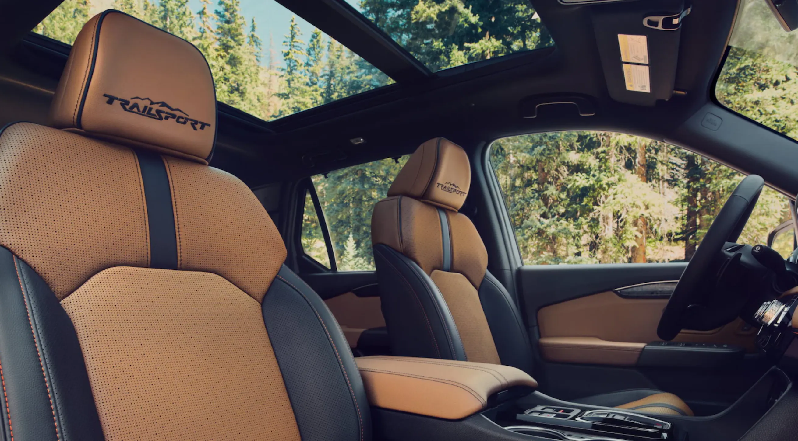 Honda TrailSport interior featuring tan leather front seats with embroidered headrests and a panoramic roof overlooking a forest.