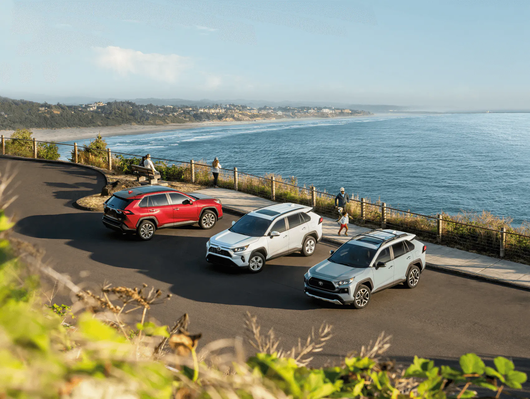 A row of Toyota vehciles sit parked on a hill overlooking a coastline.