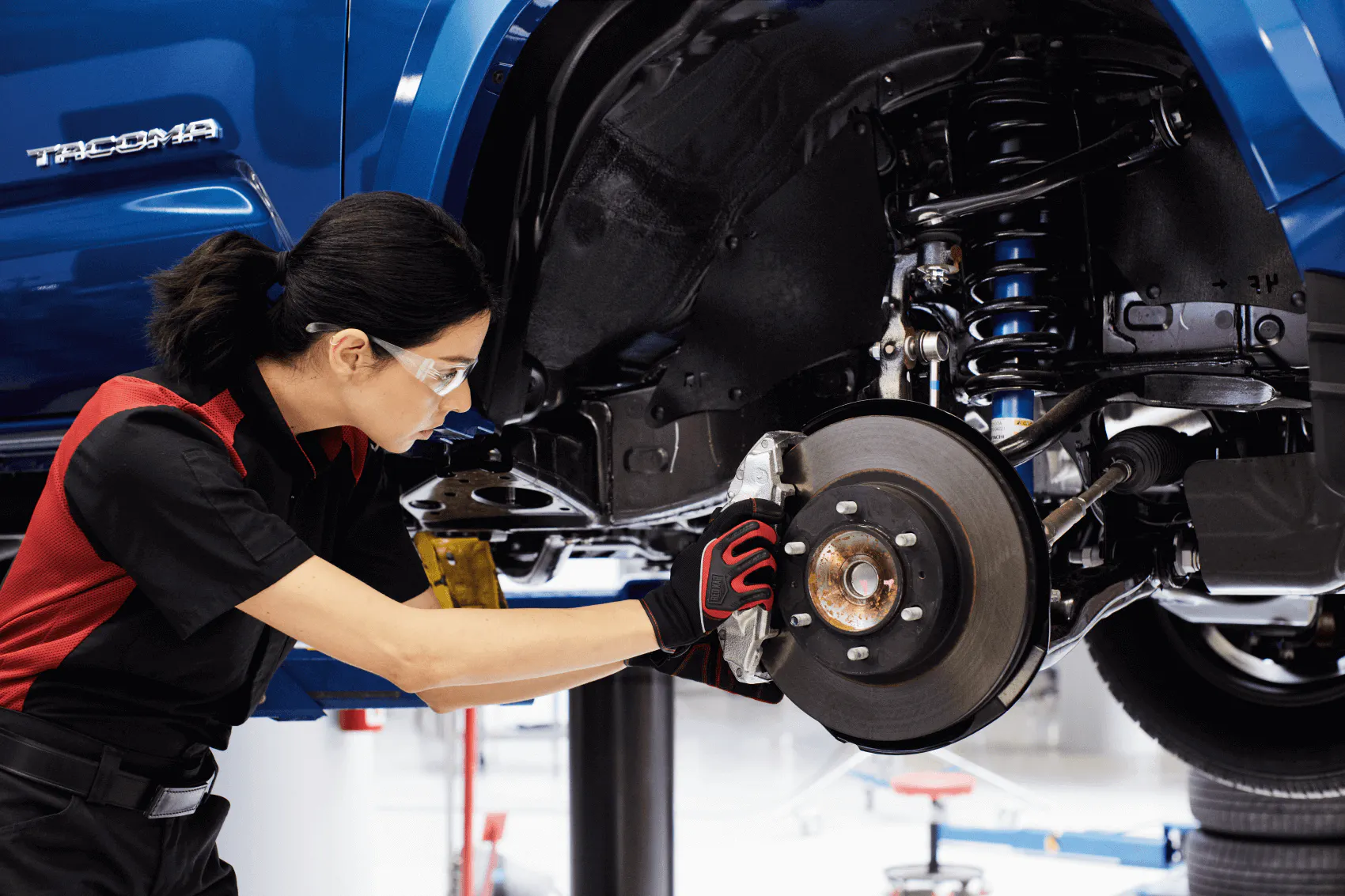 A female Toyota technican works on the brakes of a Blue Toyota.