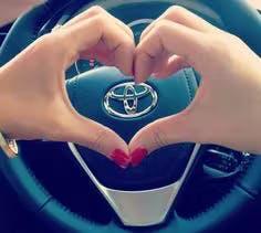 Female with red finger names hands heart with her hands over a Toyota steering wheel