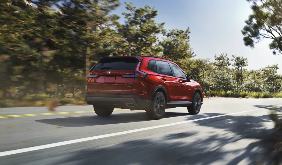Red Honda SUV driving along a sunlit, tree-lined road with motion blur emphasizing movement and speed.