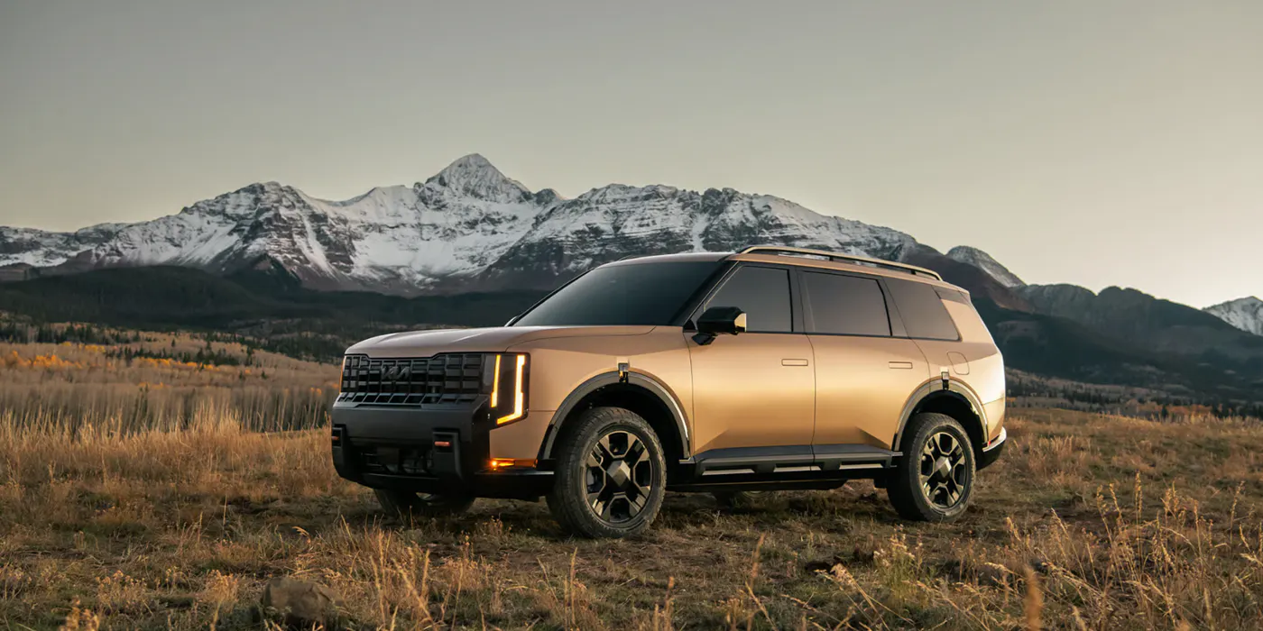 Gold Kia Telluride SUV parked in an open field with snow-capped mountains in the background during golden hour.