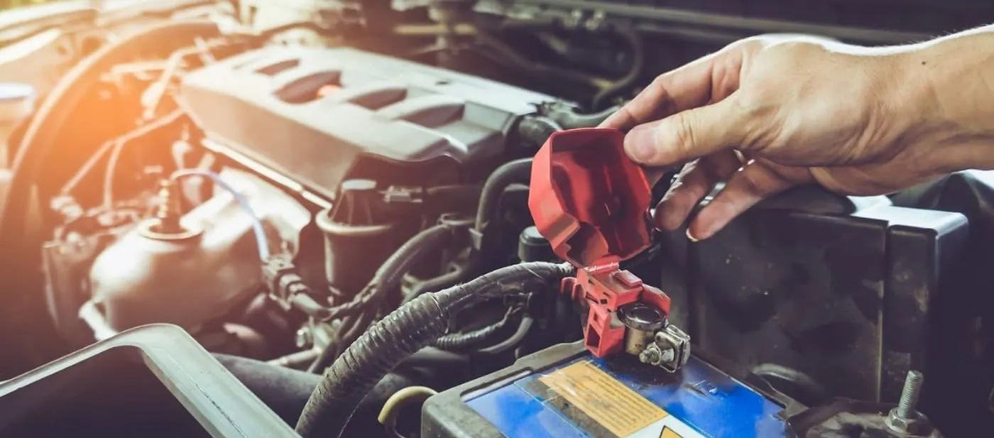 Close-up of a technician disconnecting a vehicle battery terminal under the hood during a battery inspection or replacement service.