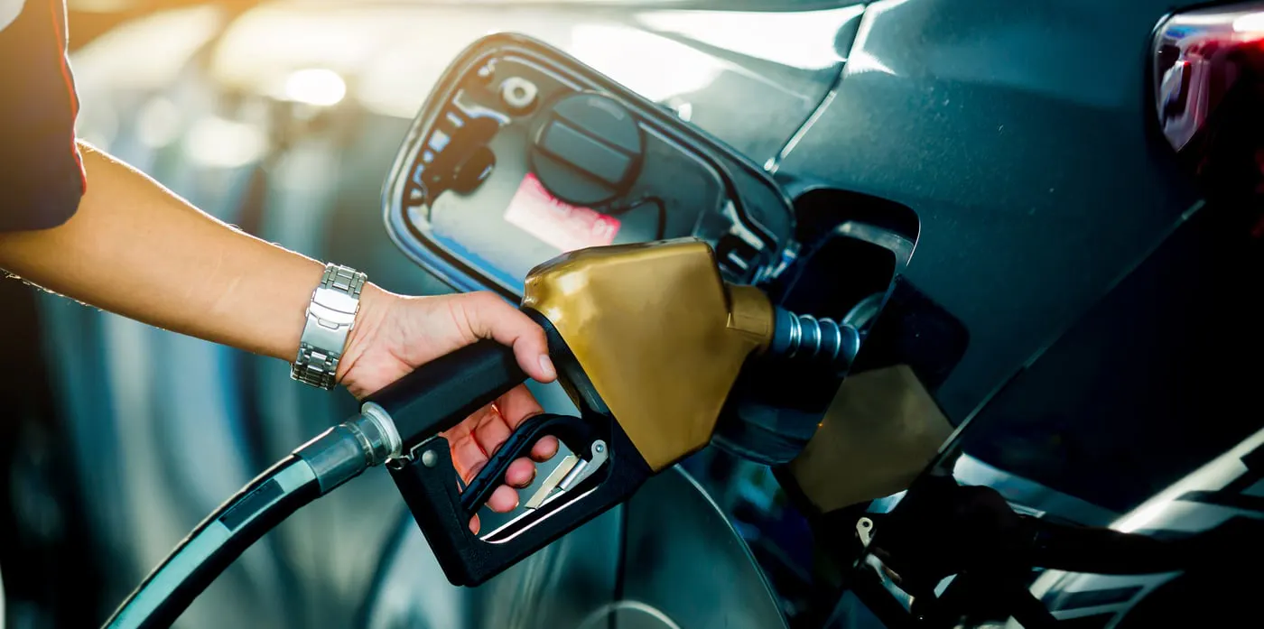 Close-up of a person refueling a Kia vehicle at a gas station by inserting a fuel pump nozzle into the open fuel filler.