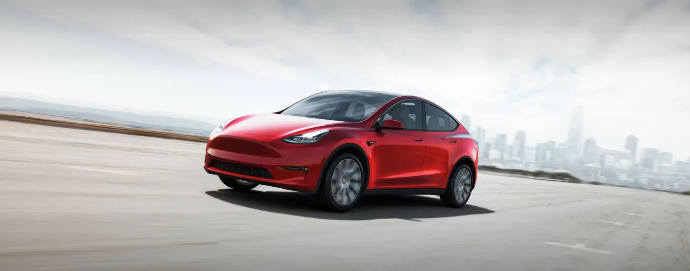 Red 2021 Tesla Model Y driving from a city.