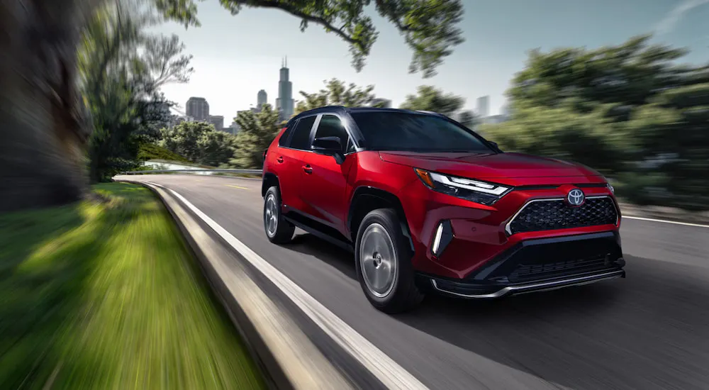 Red 2026 Toyota RAV4 PHEV driving down a road.
