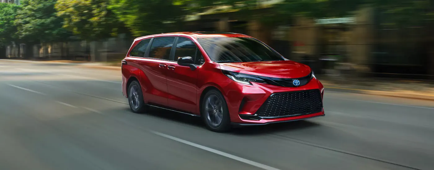 Red 2025 Toyota Sienna driving down a city street.