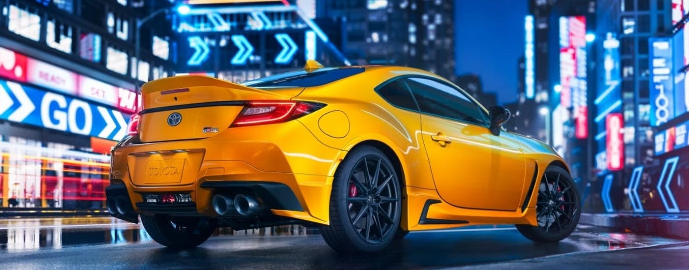 A yellow 2026 Toyota GR86 Yuzu from the rear at an angle after leaving a Toyota service center.