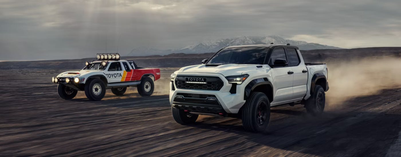 White 2026 Toyota Tacoma driving off-road next to a rally truck