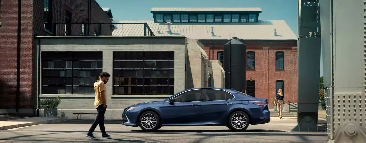 A person walking up to a blue 2023 Toyota Camry parked on a city street