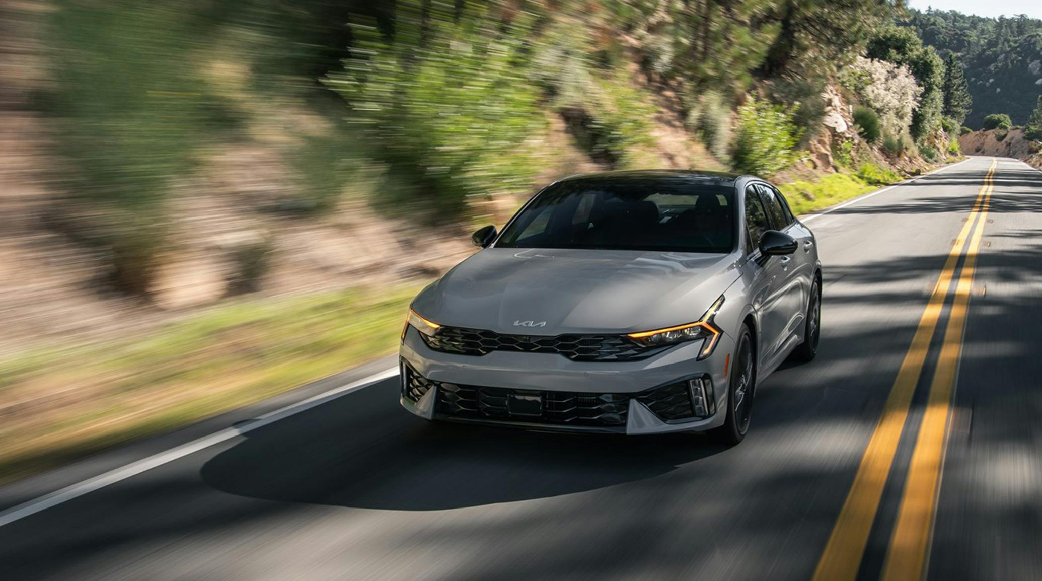 kia k5 grey driving down a mount road