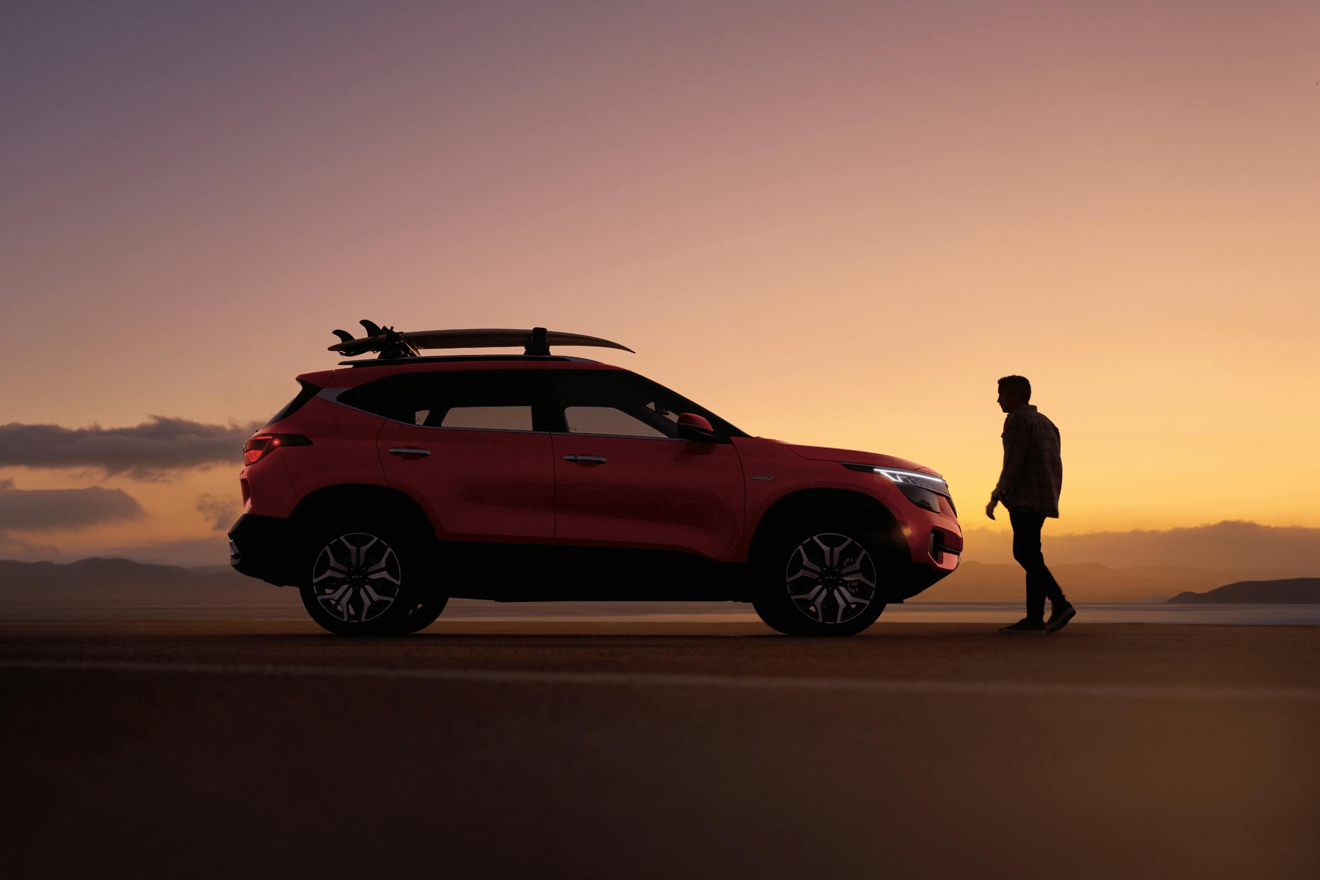 kia seltos at sunset with a man walking to it on the beach