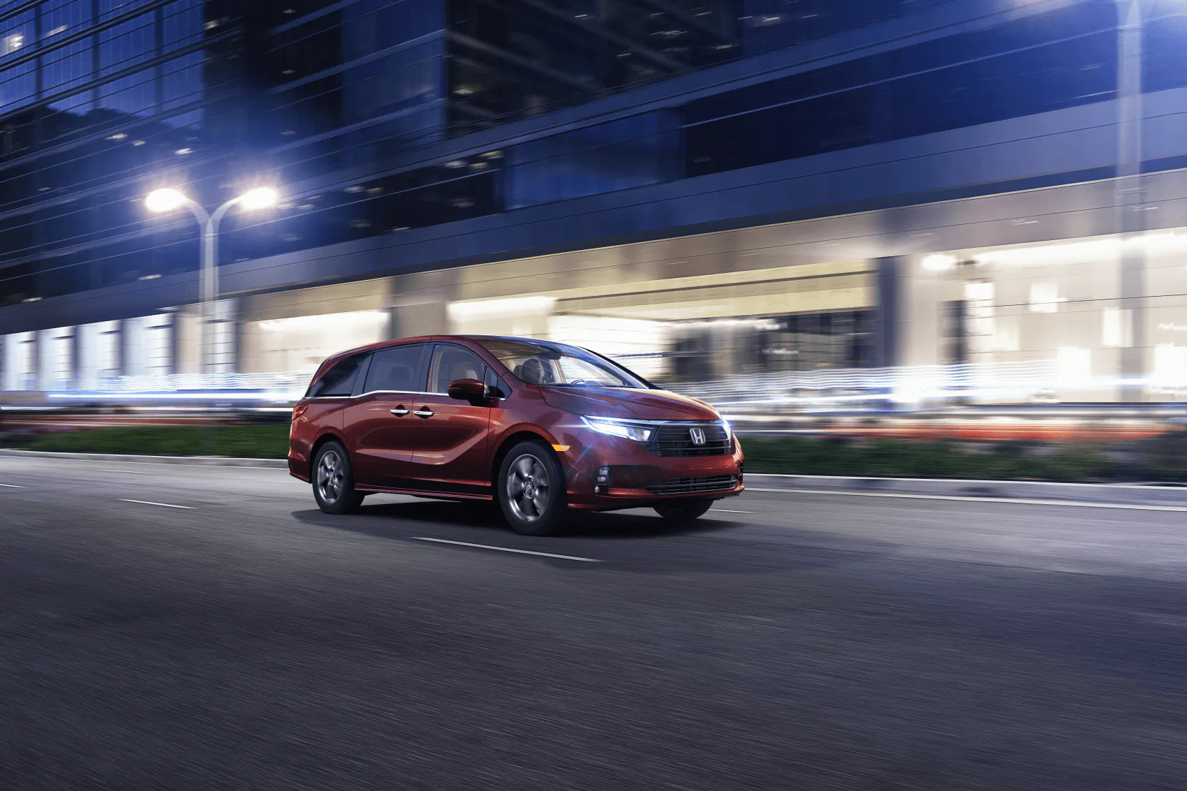 A red 2024 Honda Odyssey drives through a city at night.