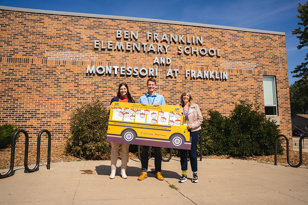 three adults smiling in front of school