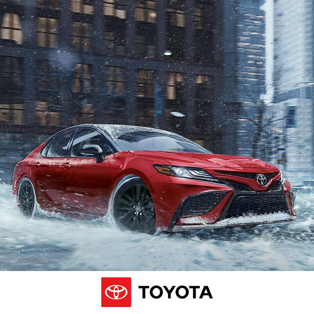 Image of red Toyota Camry driving through city street with snow and ice