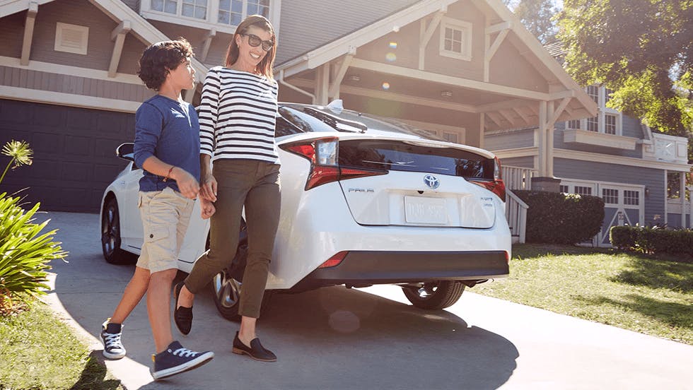 mom and son smiling by a white sedan