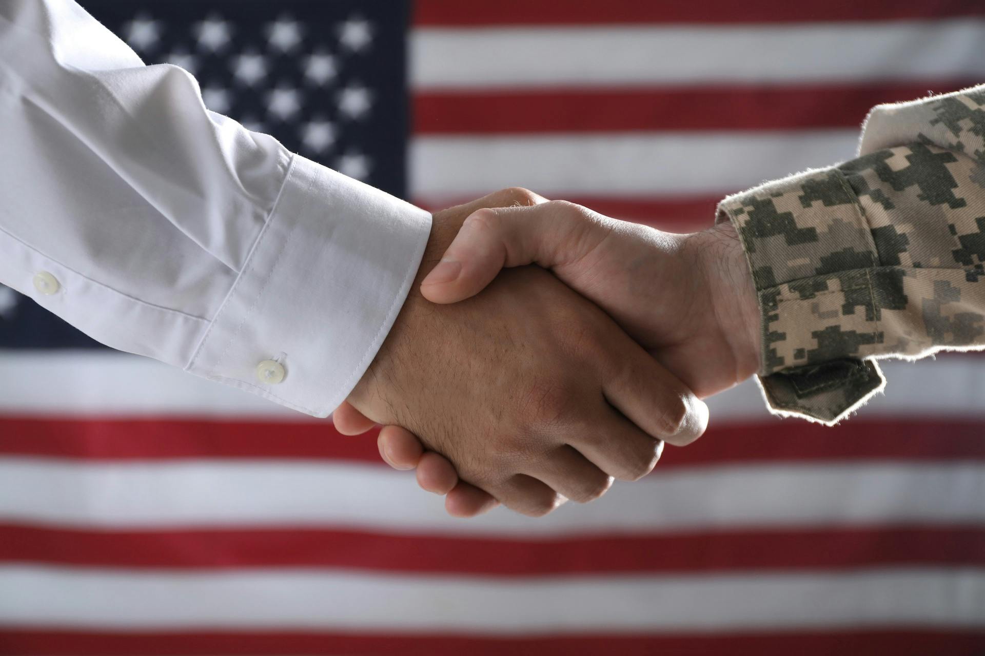 Soldier and businessman shaking hands against flag of USA, closeup