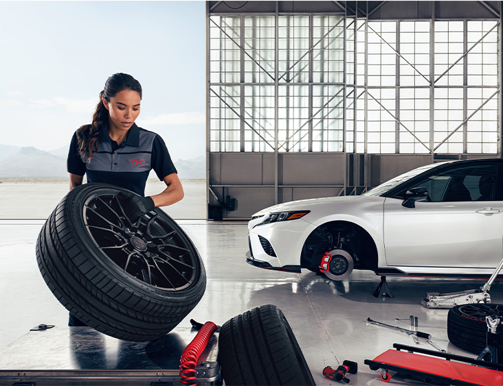 3 Main Benefits of Using OEM parts for your vehicle at Team Toyota of Glen Mills in Glen Mills, PA | Female mechanic holding new wheels with tires for the white Camry in the background 